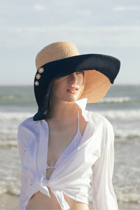 Romy wide brim hat from natural raffia and black cotton canvas At the beach